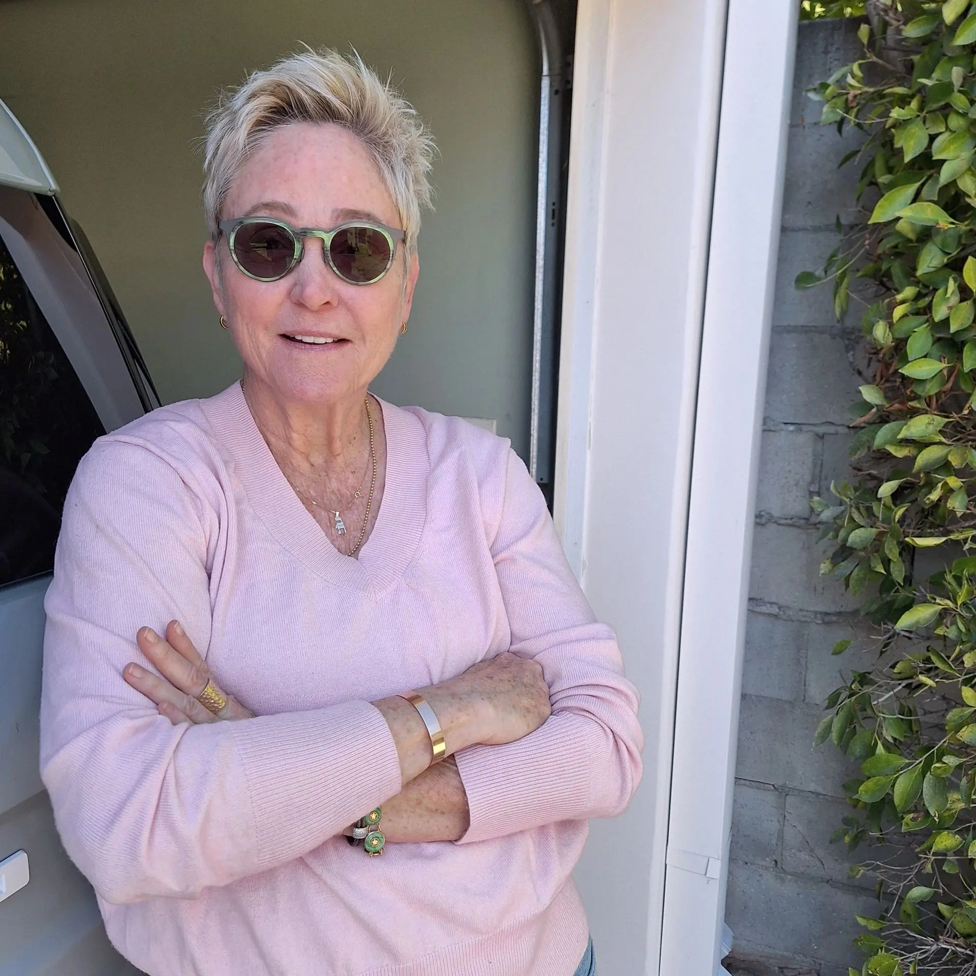 Person wearing sunglasses, pink sweater, smiling.